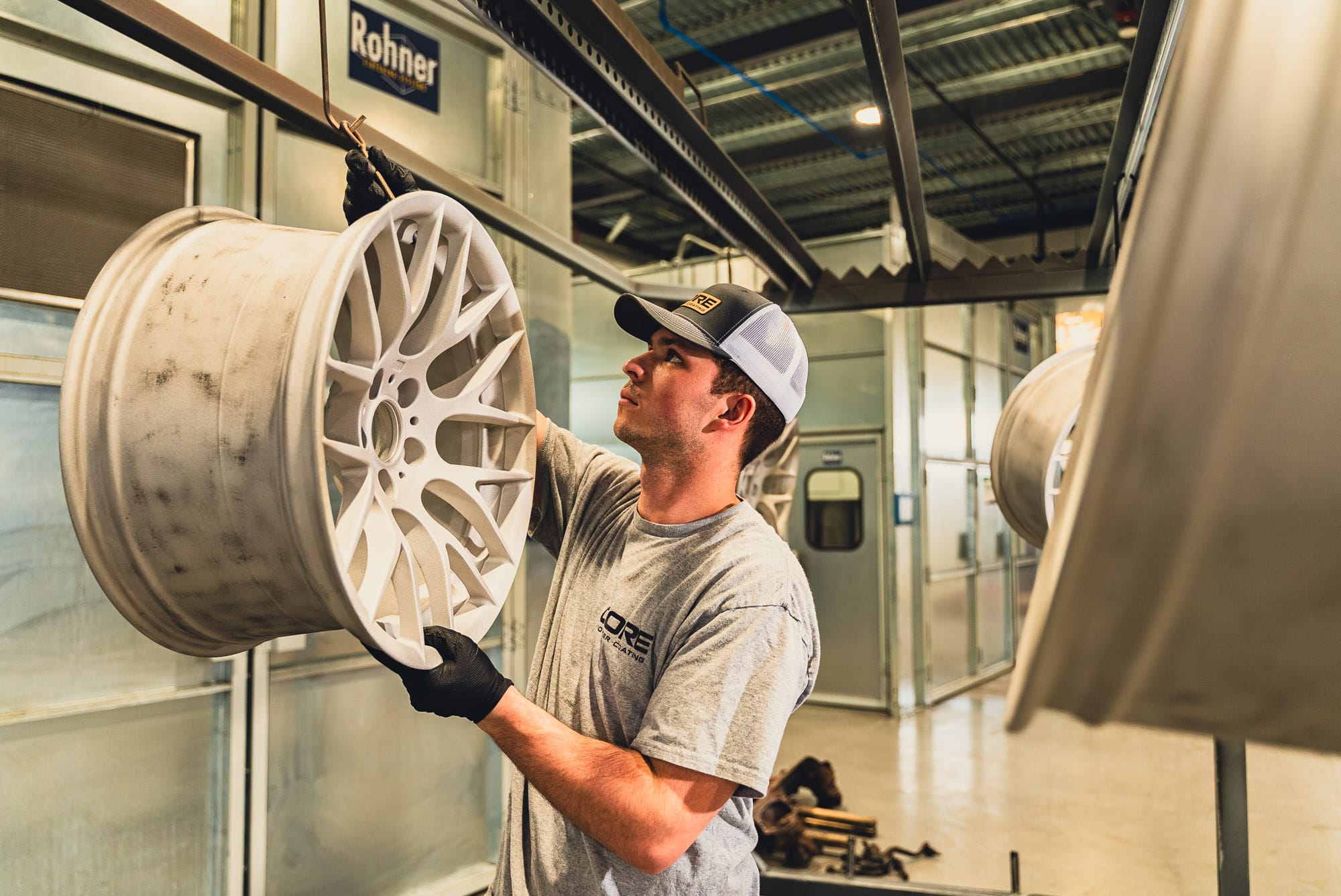 Worker inspecting alloy wheel in paint booth