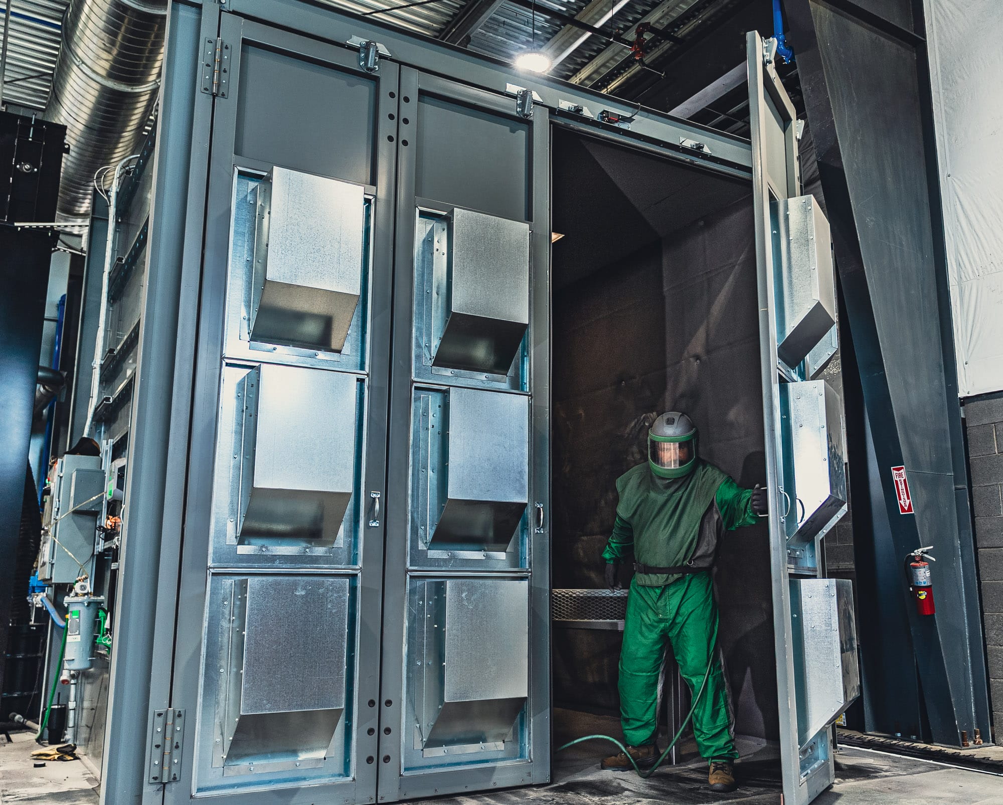 Worker in protective suit inside industrial blasting booth