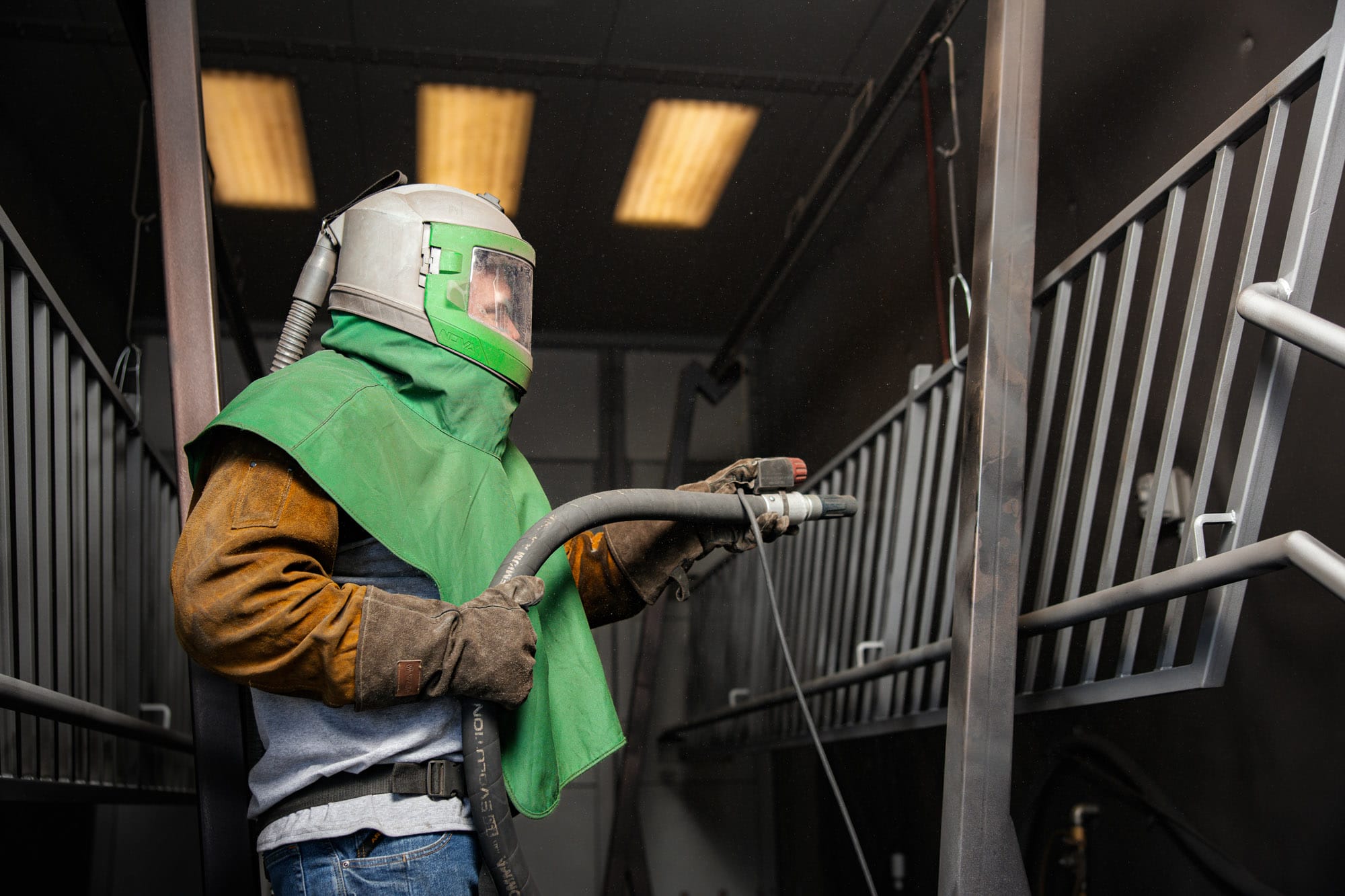 Worker sandblasting metal railing wearing protective gear