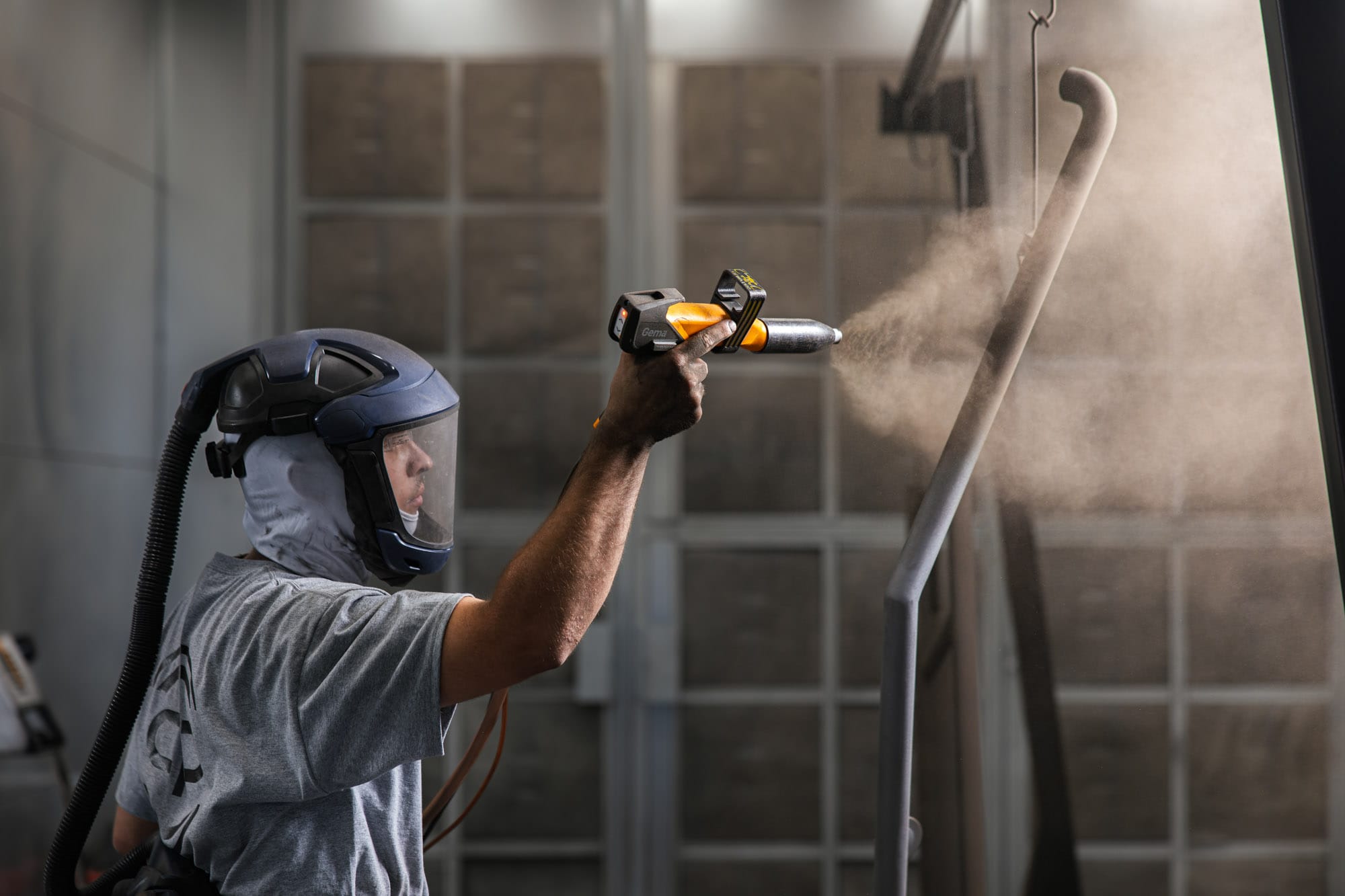 Worker wearing respirator spray painting metal frame indoors