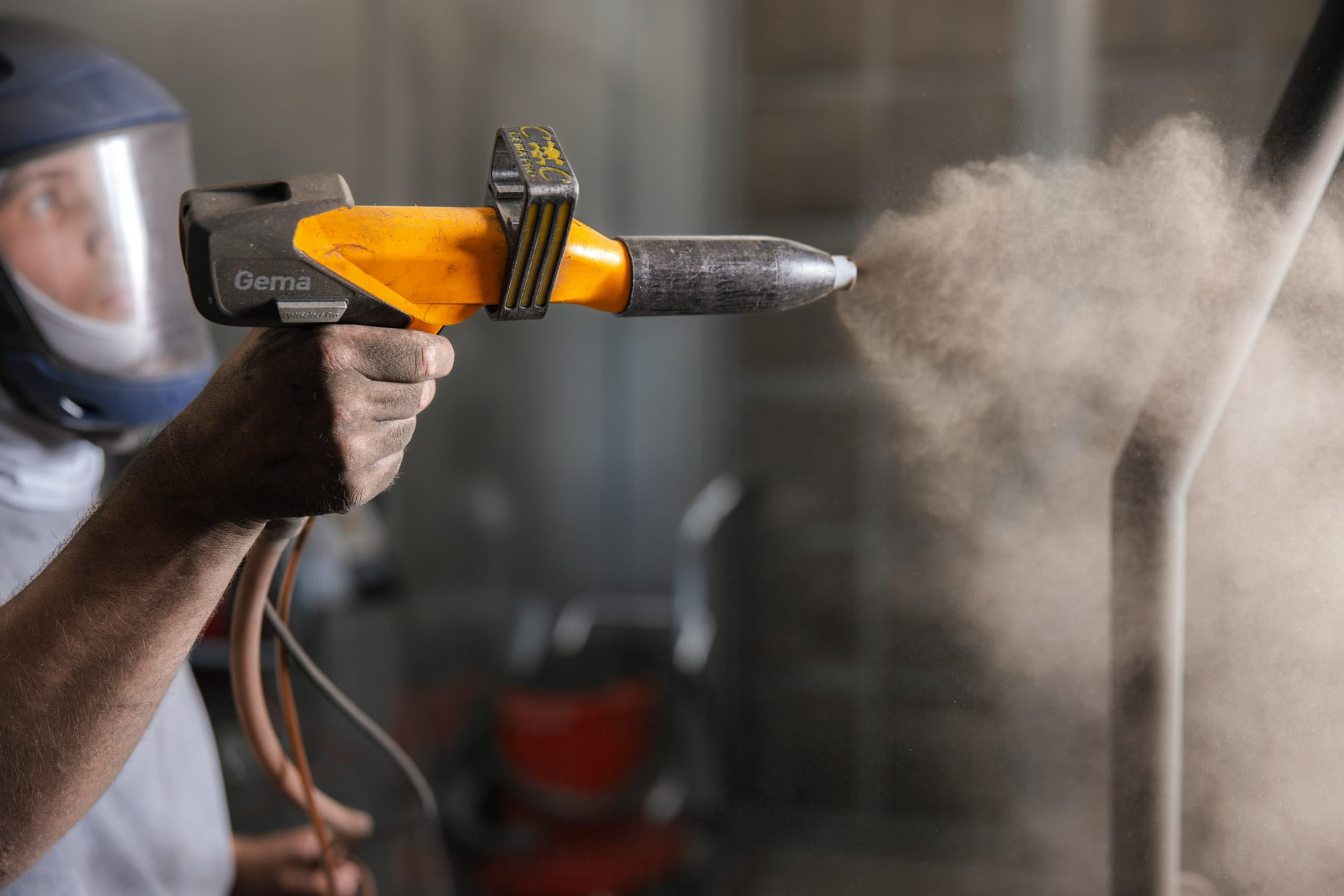 Worker powder coating metal surface with spray gun