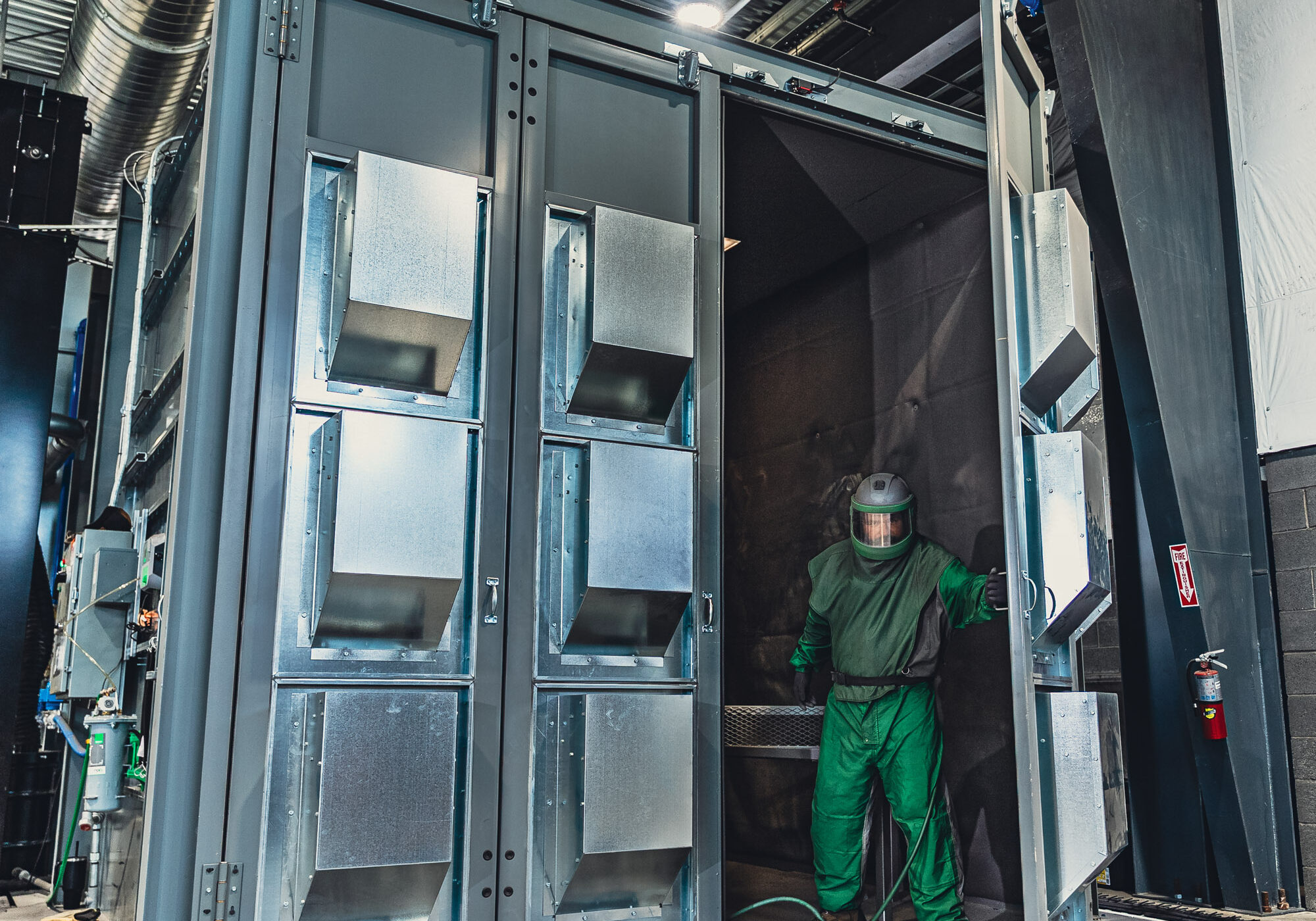 Worker in protective suit inside industrial blasting booth