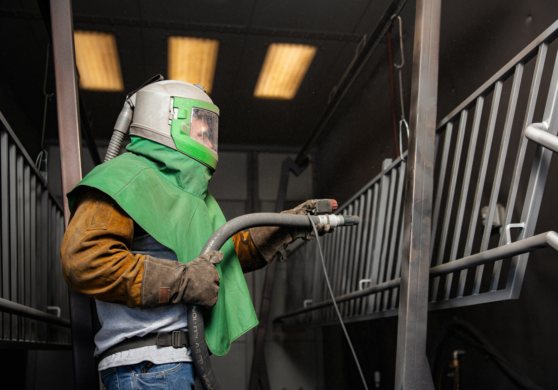 Worker sandblasting metal railing wearing protective gear